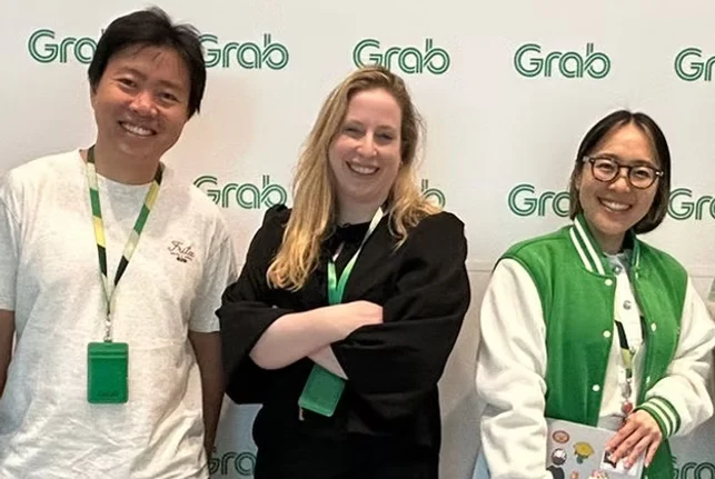 Mikka with two members of the Grab team in front of a Grab logo wall in Singapore